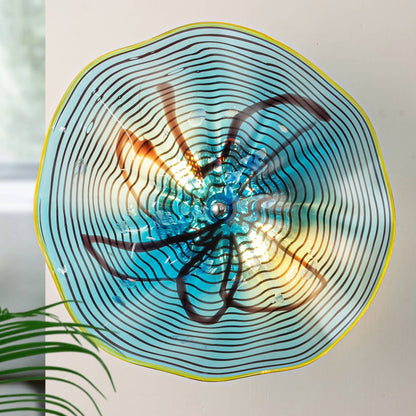 Close-up of a 12-inch aqua glass wall sconce with yellow rim and black ink pattern lit by G9 LED bulbs.
