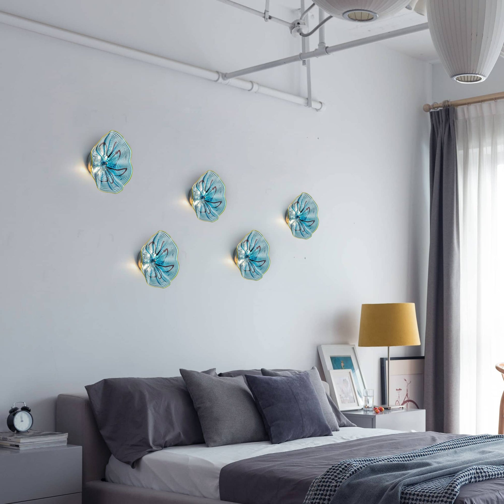 Creative bedroom wall display featuring multiple aqua and ink pattern glass art lights above a bed.