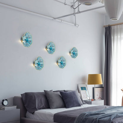 Creative bedroom wall display featuring multiple aqua and ink pattern glass art lights above a bed.