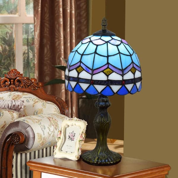 Blue stained glass lamp glowing on a side table next to a classic sofa and picture frame.
